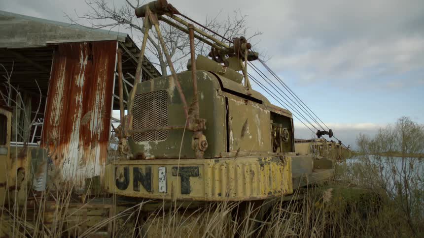 An old rusty barn and a broken down crane sit next to a pond on a cloudy day