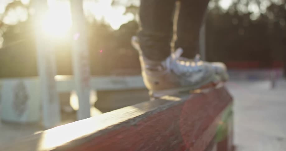 A person in roller skates slides across a wooden rail in a skate park during the day