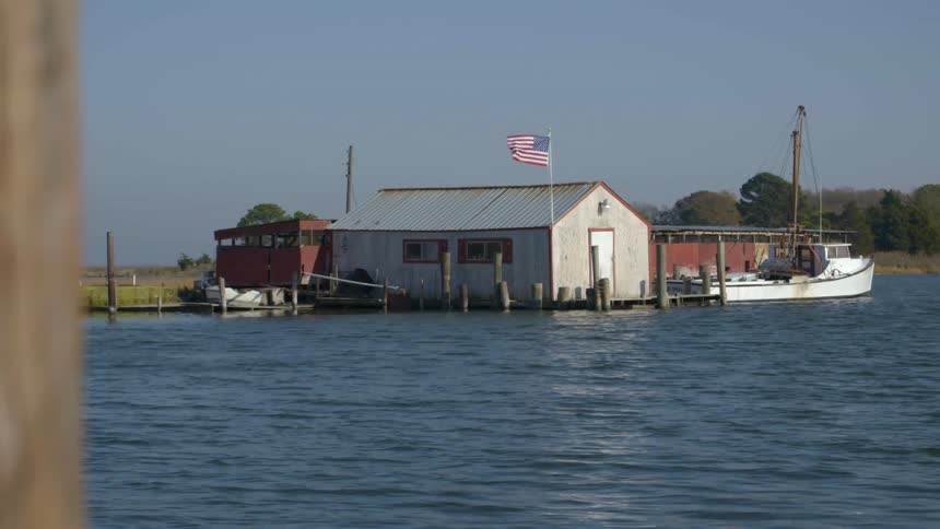 American flag waves in wind above a fishing shack and fishing boats
