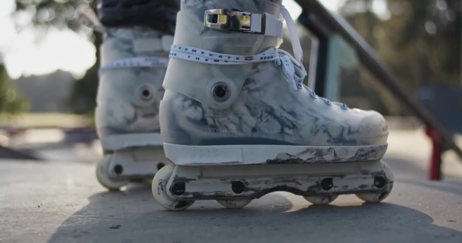 A person in a skate park standing in inline skates with trees the sky and clouds in the background