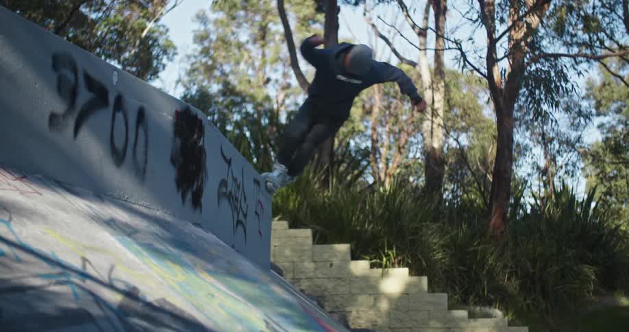 A person with inline skates grinding on a wall in a skate park with trees the sky and clouds in the background