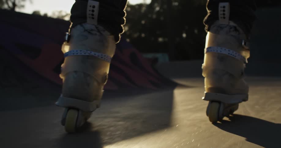 A person with inline skates skating in a skate park with trees the sky and clouds in the background