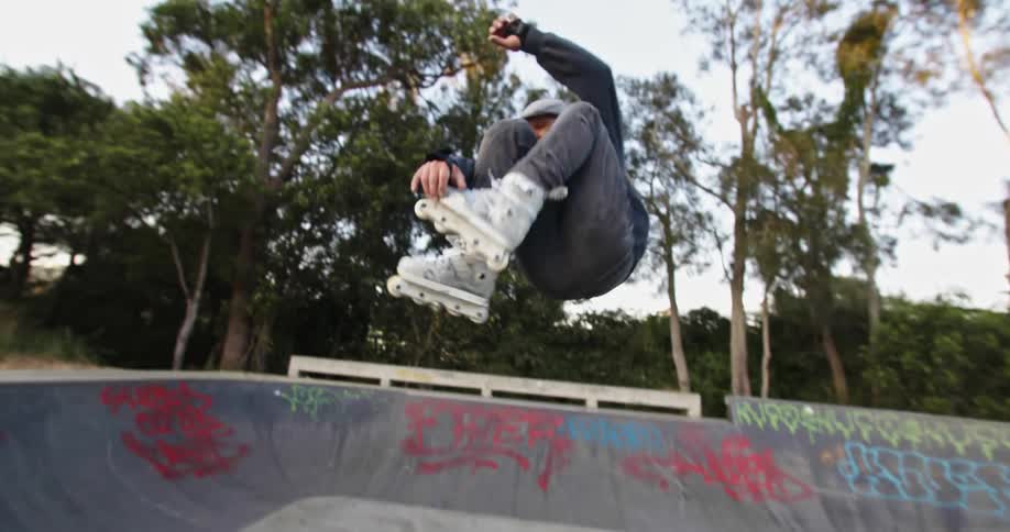 Older man roller blades up a rollerblade ramp then jumps and spins around and roller blades back across the ramp