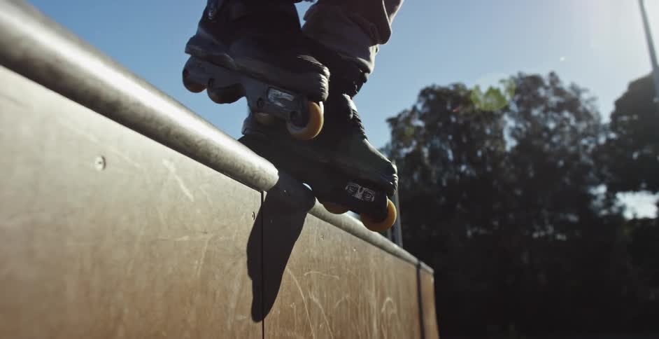 A roller skater steps towards the edge of a ramp platform and rolls off outdoors at daytime