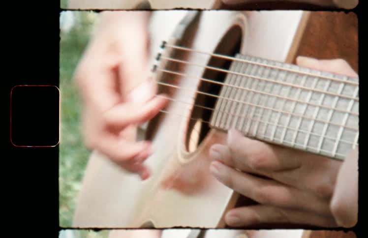 Film footage of woman placing a mans hands on a guitar strings