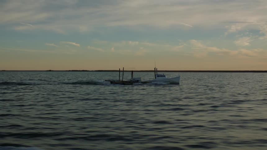 A fishing boat motoring across the water at sunset