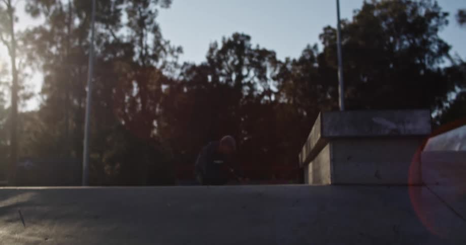 A man wearing inline skates performs a jump on a ramp at a skateboard park in the morning