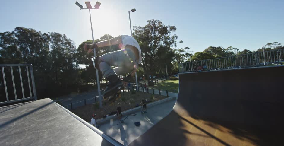 Teenager roller blades up a ramp then spins around in the air and falls down