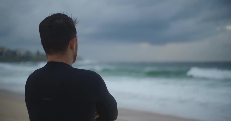 A man standing at the shore pointing out towards the ocean in the evening