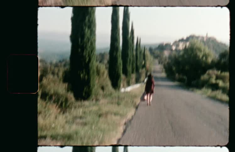 Woman in a red dress walking on a road in the countryside caught on vintage film
