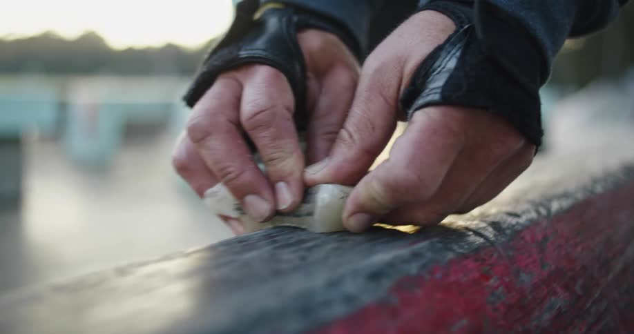 Close up of a man waxing a skateboard railing in the park at sunset