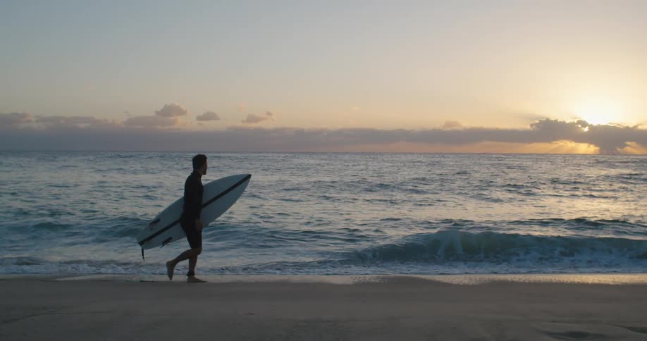 A man with a wet suit holding a surfboard on a beach with the ocean sky and clouds in the background