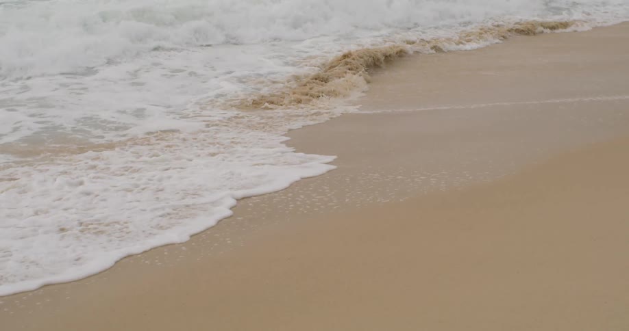 Small waves crashing over the brown beach sand