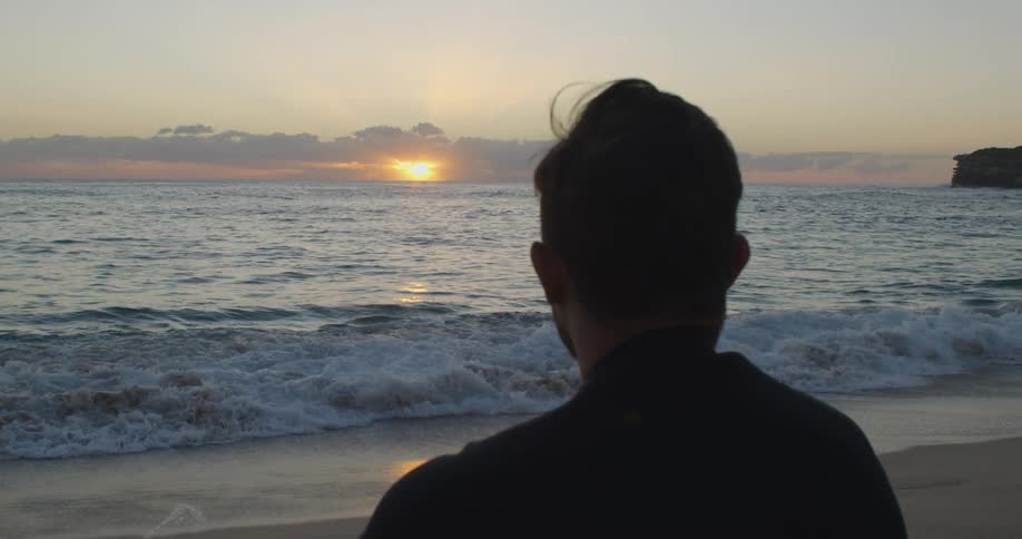 The silhouette of a man sitting on a beach watching the waves at sunset