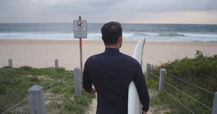 A man walks toward the beach with a surfboard under his arm