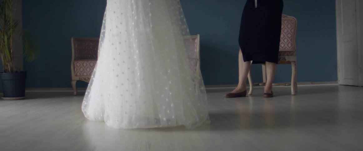 Employee stands with measuring tape around her neck watching woman try on wedding dress