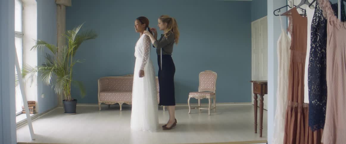 Tailor testing a long white dress on a client in her studio