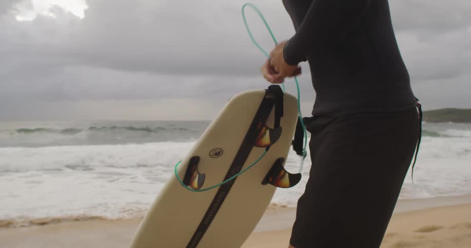 A man undoes the strap to his paddle board while standing on the beach