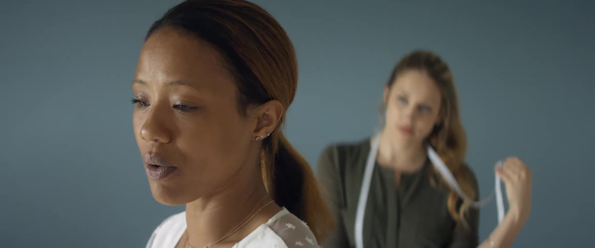 Two women in a room with one with a measuring tape with a wall in the background