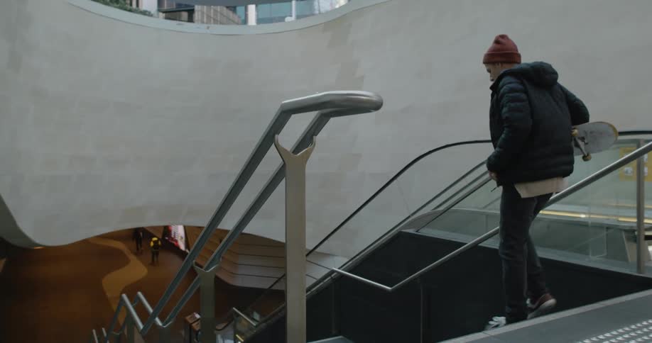 A man rides his skateboard to the stairs then picks it up and runs down the stairway
