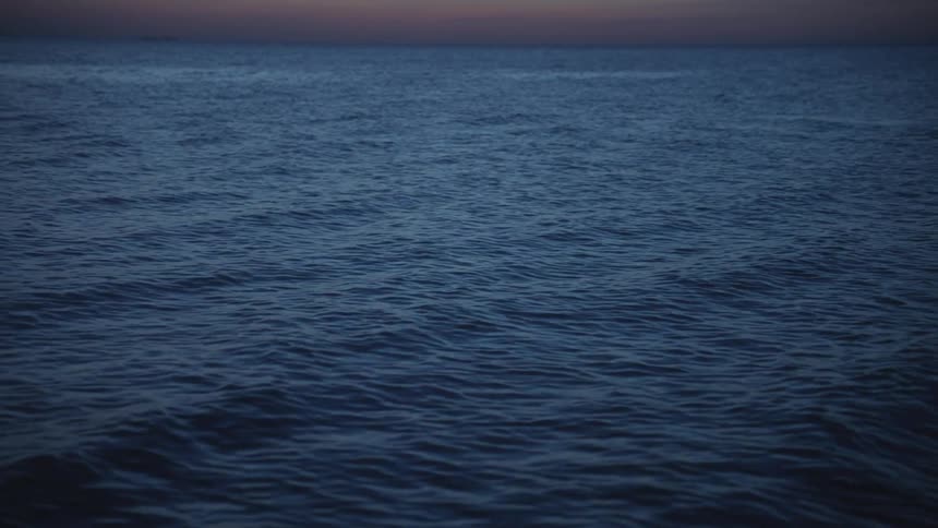 Waves roll over dark blue water with shore in distance