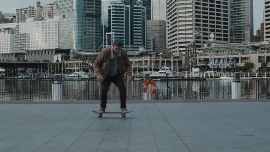 A teenage boy skateboards on the boardwalk next to the shore