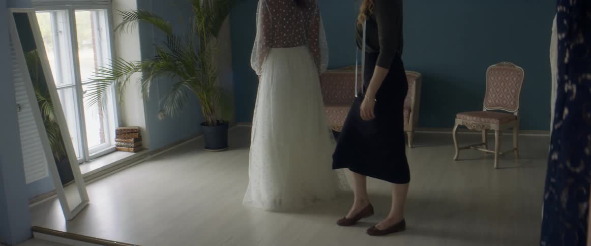 Two women in a room with one with a measuring tape with a wall and window in the background