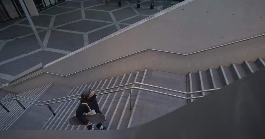 A man walks up a large empty staircase carrying a skateboard and a bag