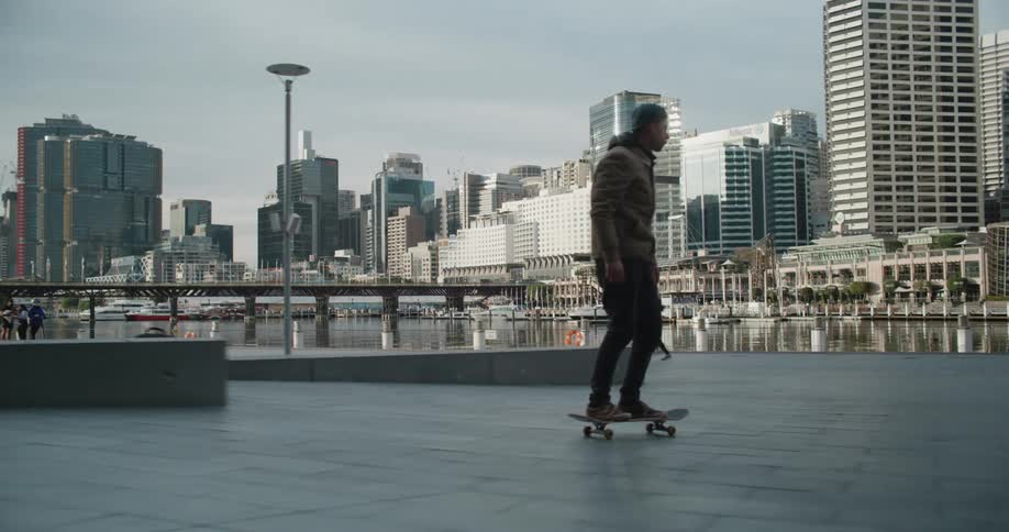 A man rides his skateboard and jumps off concrete barriers as he makes his way along a boardwalk in a downtown urban area