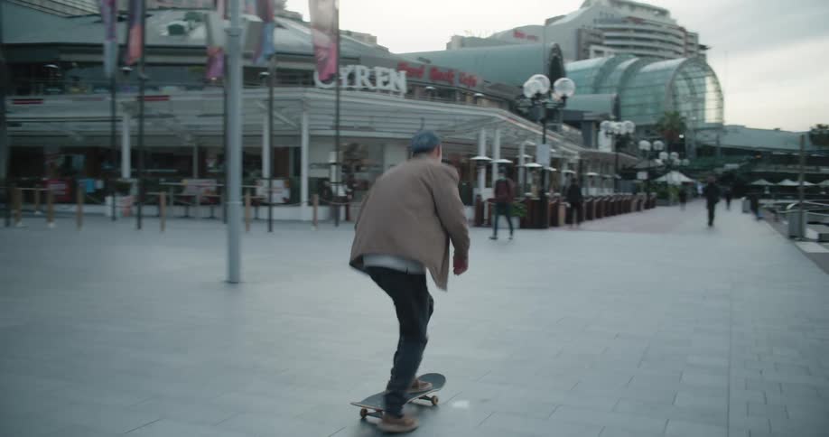 A man skating on a skateboard on a boardwalk with ferris wheel buildings the sky and clouds in the background