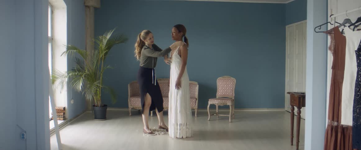 A woman is helping another woman try on a wedding dress
