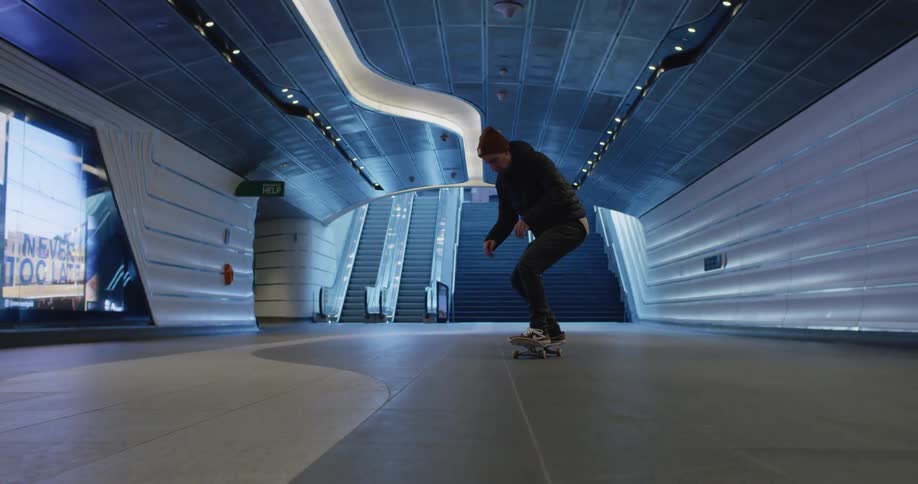 A man with his skateboard skating in a tunnel with stairs and escalators in the background