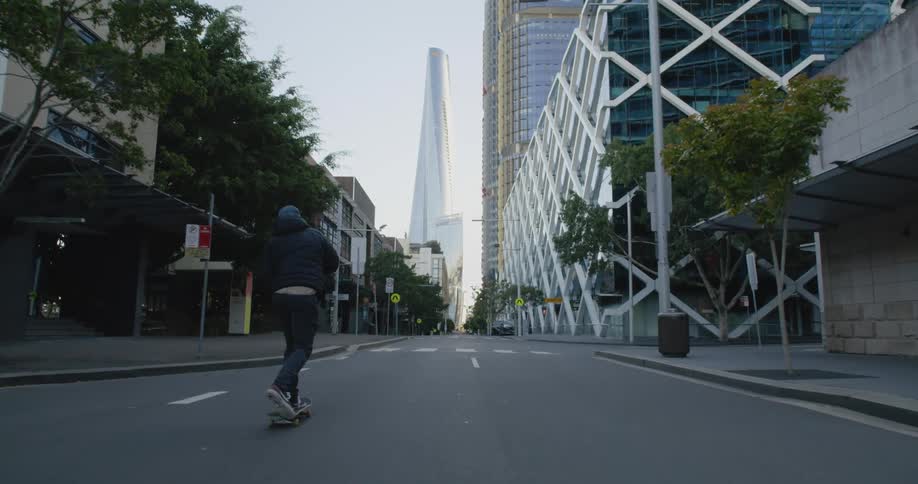 A man skating on a skateboard on a city street with buildings the sky and clouds in the background
