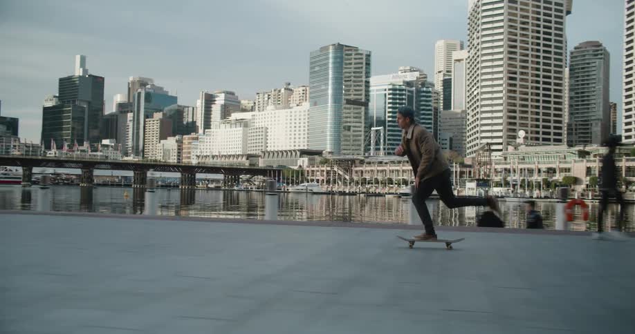A man skating on a skateboard on a boardwalk with a ferris wheel buildings the sky and clouds in the background