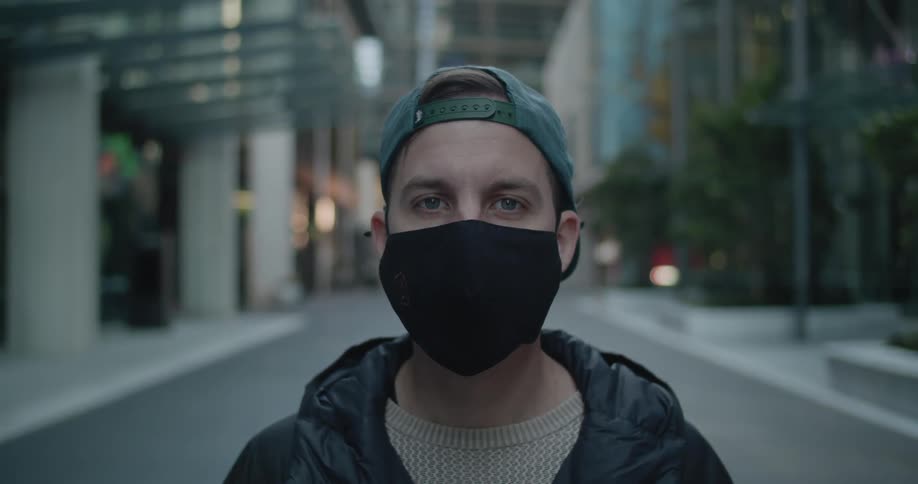 A man wearing a mask standing on an empty street lifts his head and looks straight ahead