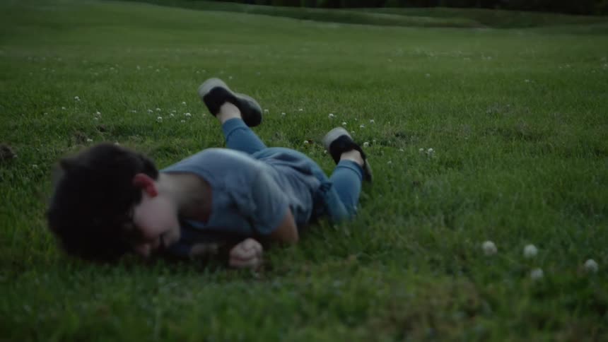 A boy rolling in grass and flowers with trees in the background