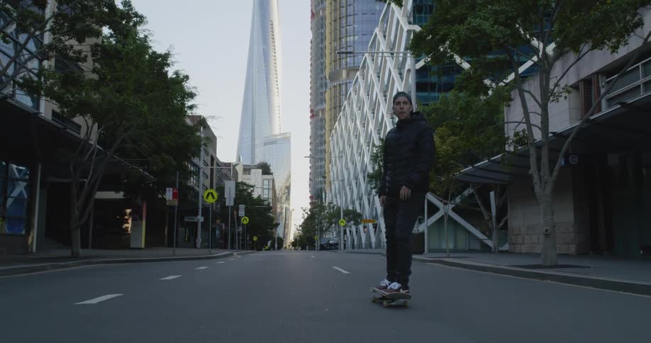 A man skating on a skateboard on a city street with buildings the sky and clouds in the background
