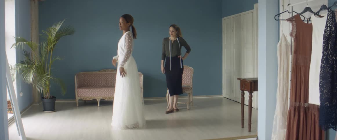 A bride to be tries on a potential dress as an employee watches