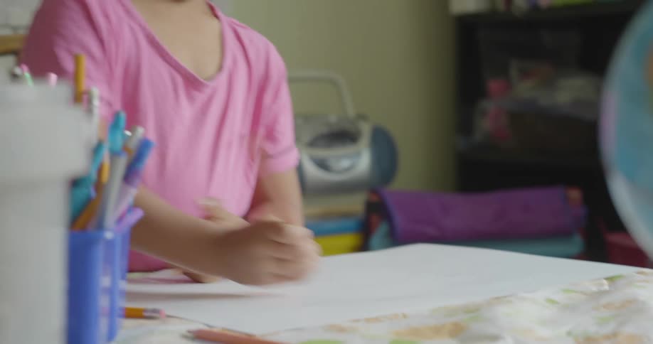 A girl sits at atable drawing on a large sheet of paper with a pencil