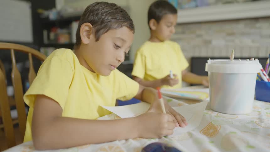 Two boys and a girl around a table drawing on papers with a wall and fireplace in the background
