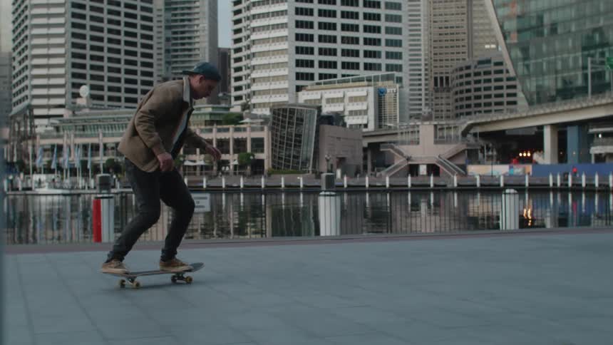 A man is skateboarding in a downtown city during midday