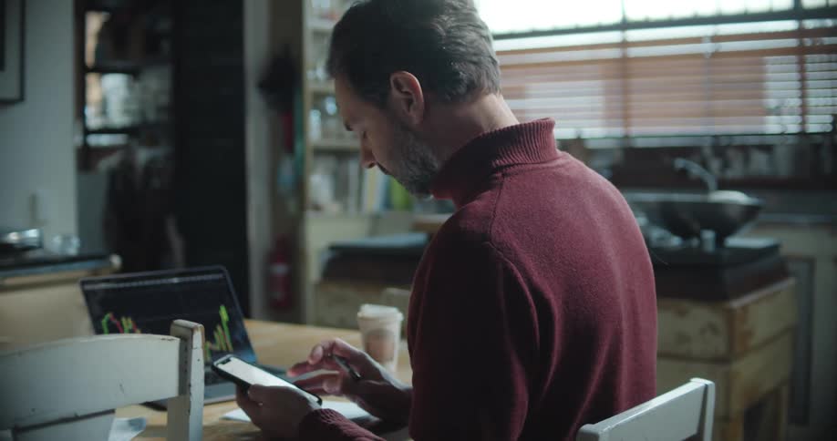 Man sitting at a desk working with a smartphone and a laptop