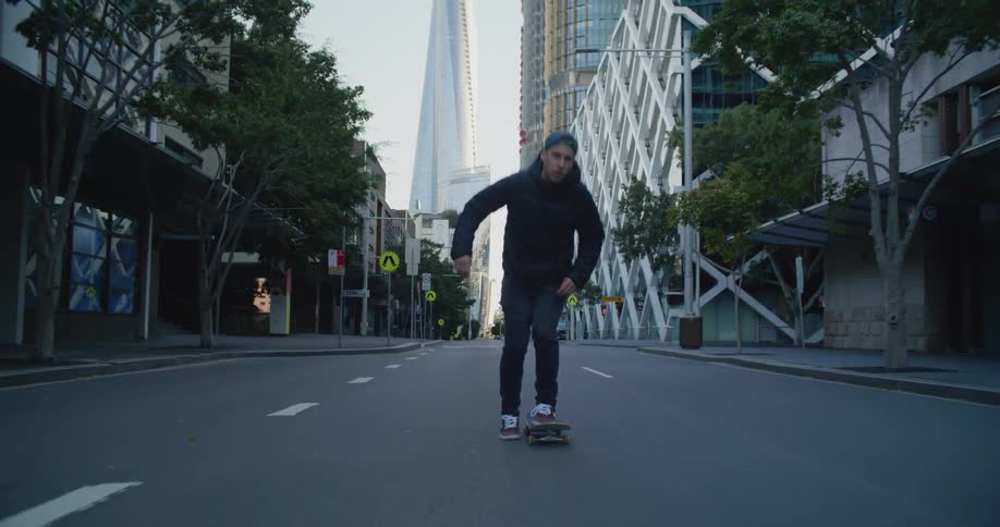 Man with cap and coat skateboards in the empty city street