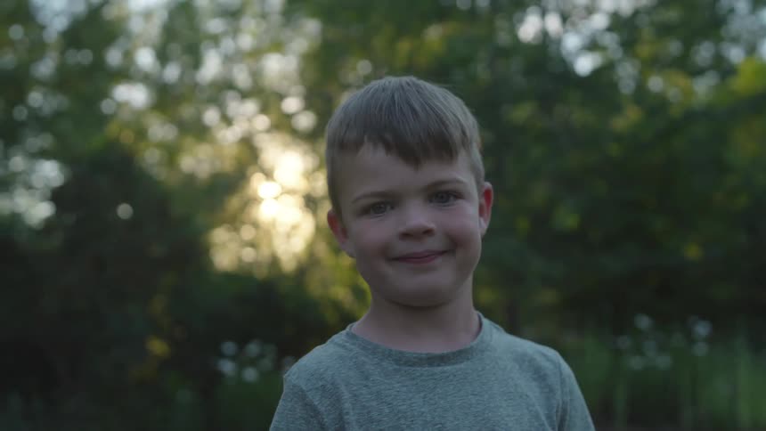 Young boy smiling at the camera in front of the trees at sunset