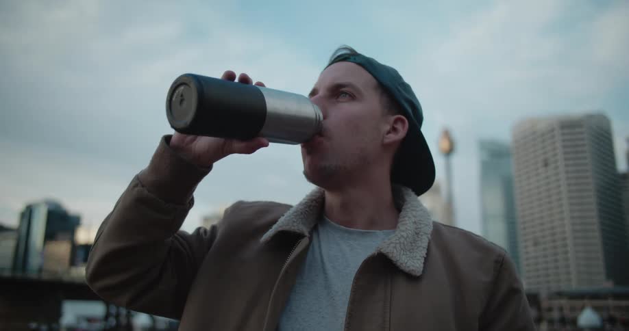 A man is drinking from a cup outdoors in a city