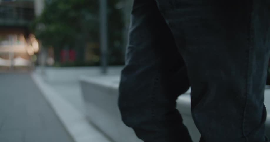 A person with jeans holding a skateboard with trees and a building in the background