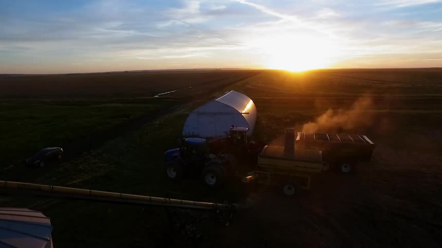Farm tractors and equipment parked near a greenhouse and fields at dusk