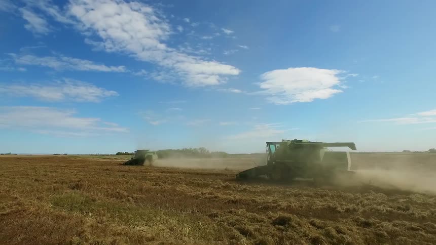 Two large pieces of moving farm equipment doing their job in a large field
