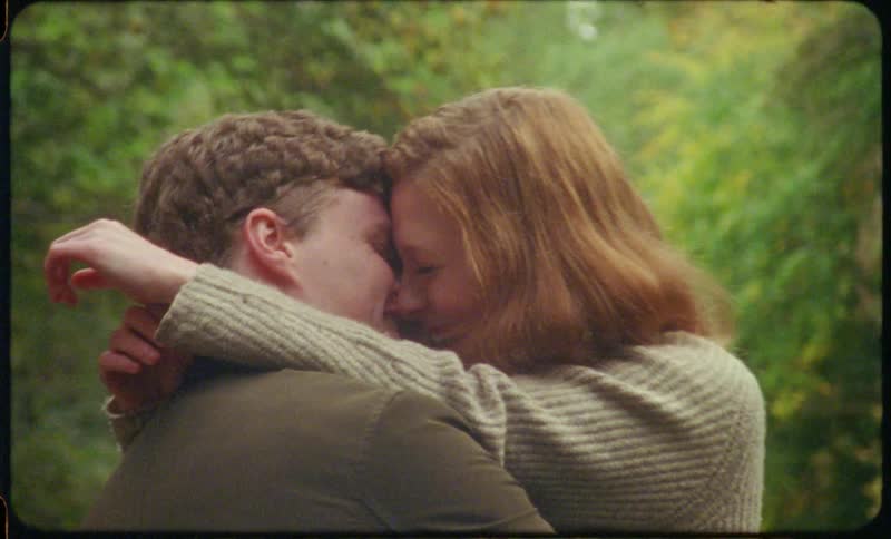 Couple smile while hugging and kissing outdoors near trees