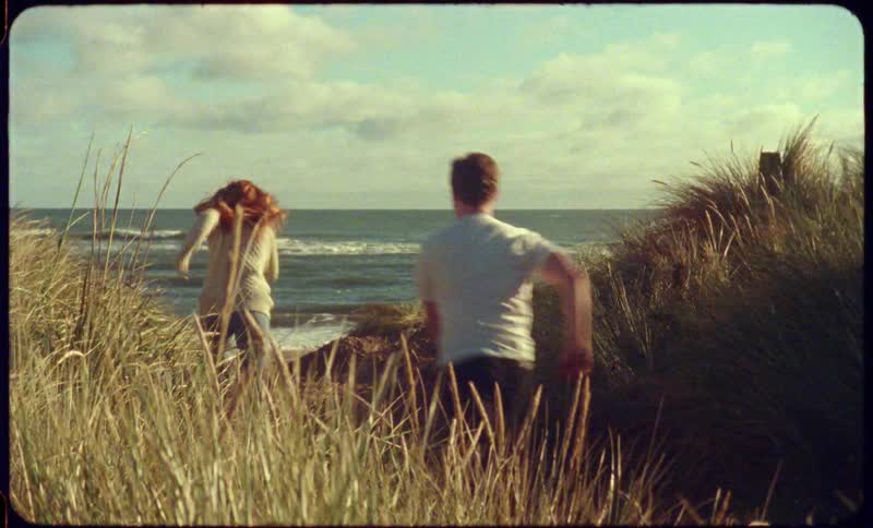 Tall grass and weeds moving in the breeze as two children run towards the beach